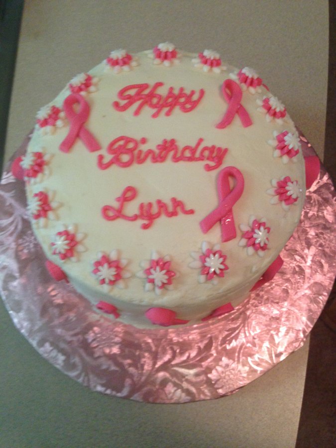 White birthday cake decorated with pink awareness ribbons and pink flowers